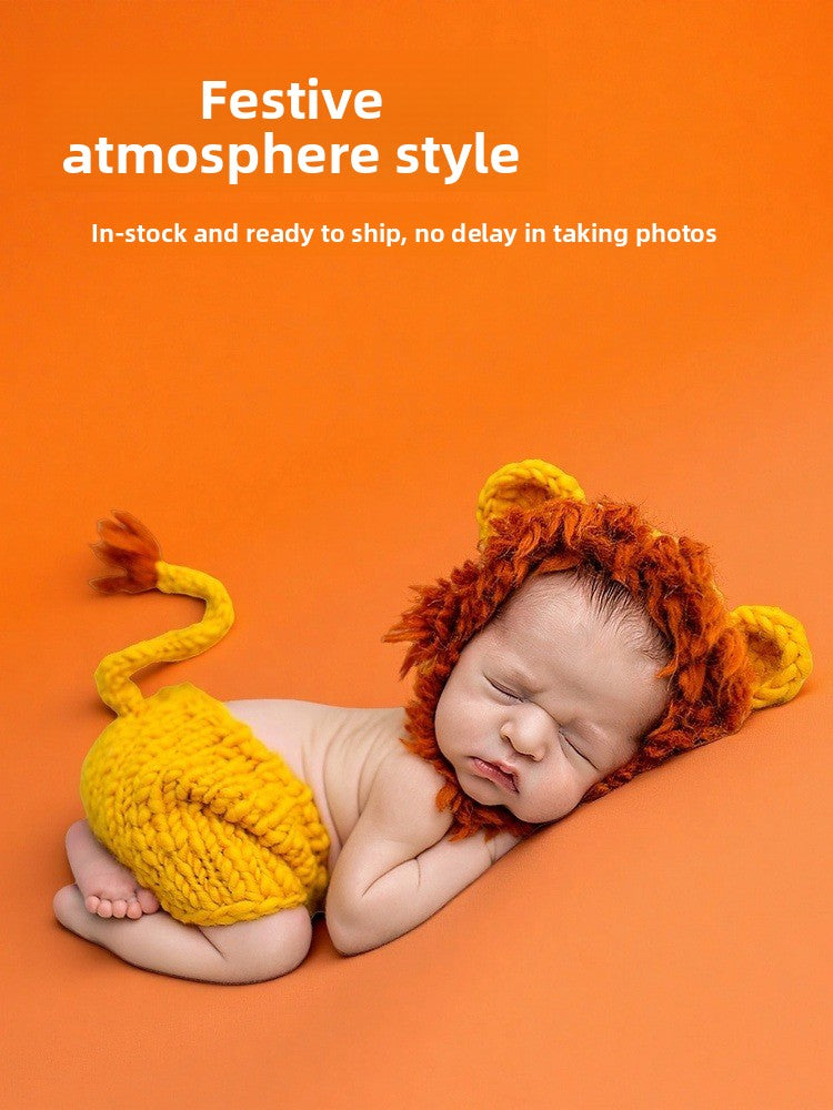 Newborn wearing an orange knit lion bonnet and shorts, curled on an orange backdrop