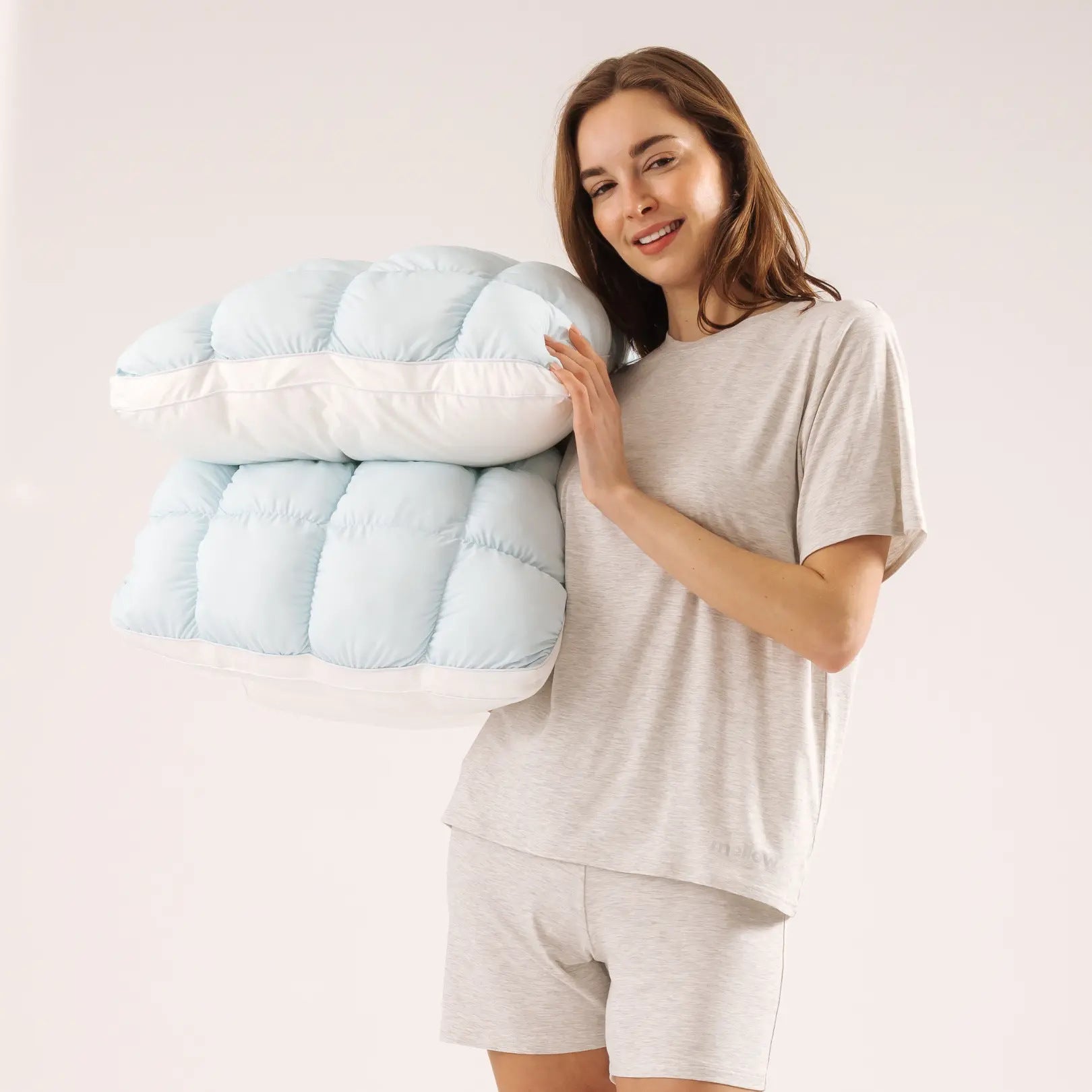 Woman holding two sky blue puff grid bed pillows against a plain studio backdrop