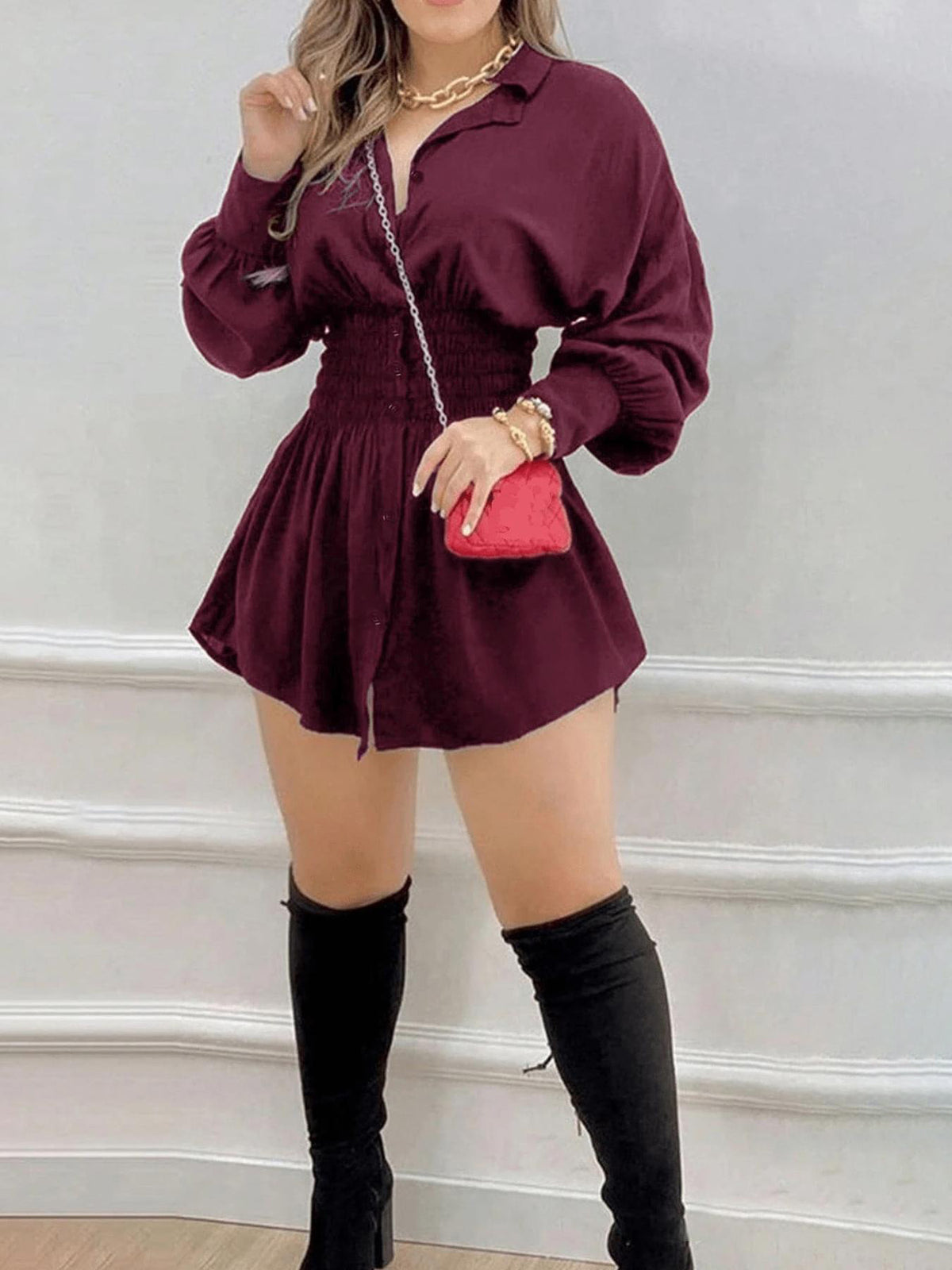 Wine red button front mini shirt dress with smocked waist and long sleeves, with tall black boots and a red bag