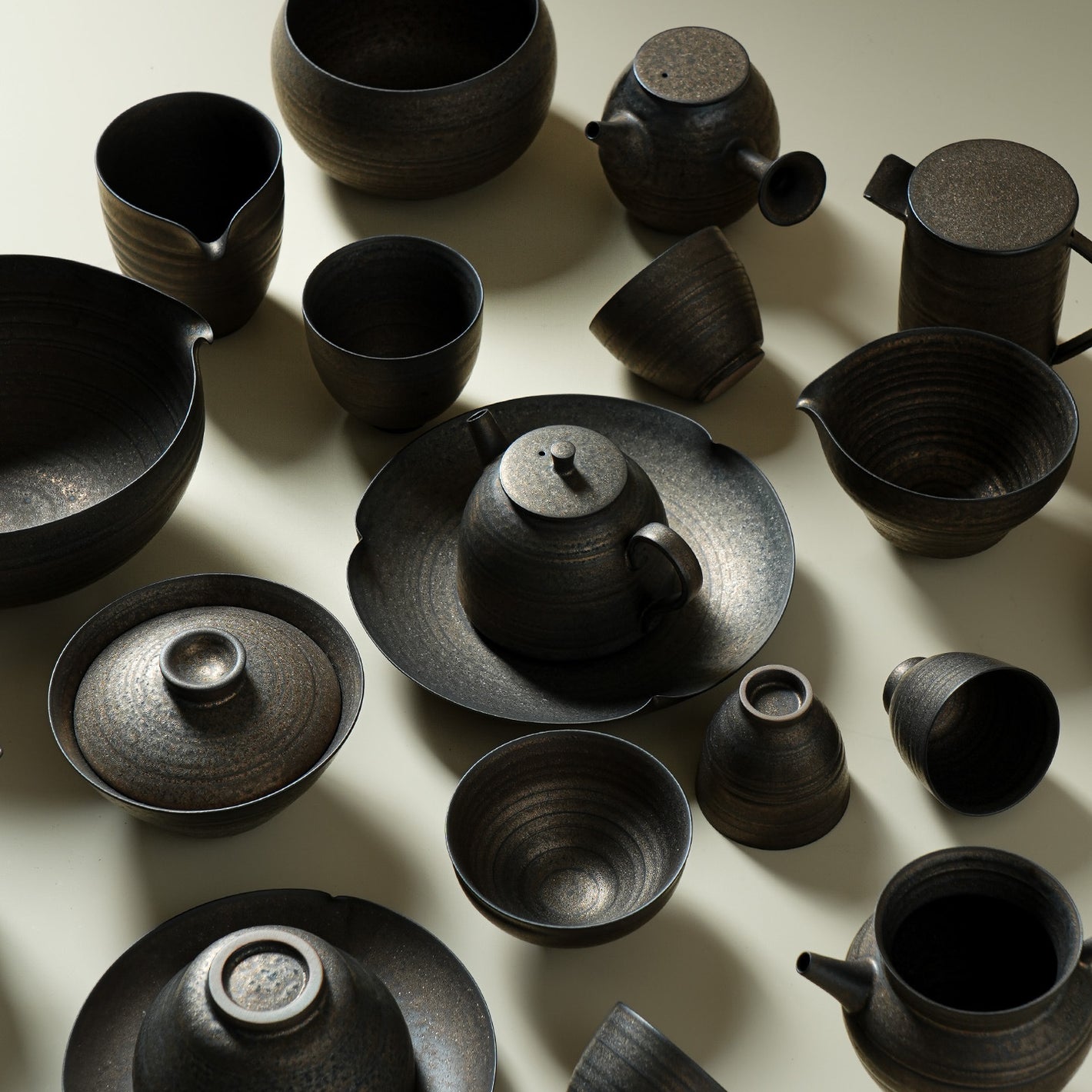 Iron glaze ceramic gongfu tea collection with teapots cups and bowls on a cream backdrop