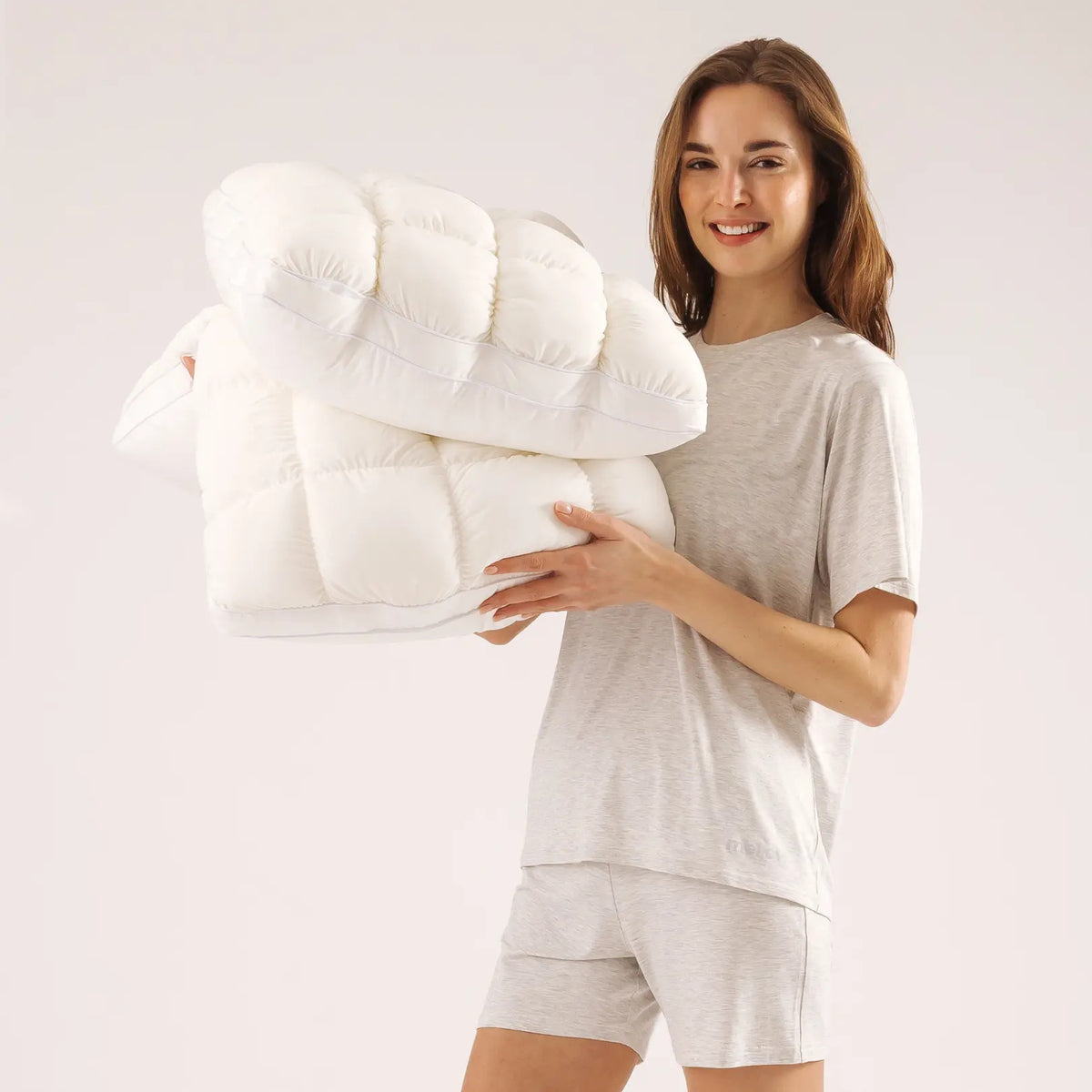 Woman holding two white puff grid bed pillows against a plain studio backdrop