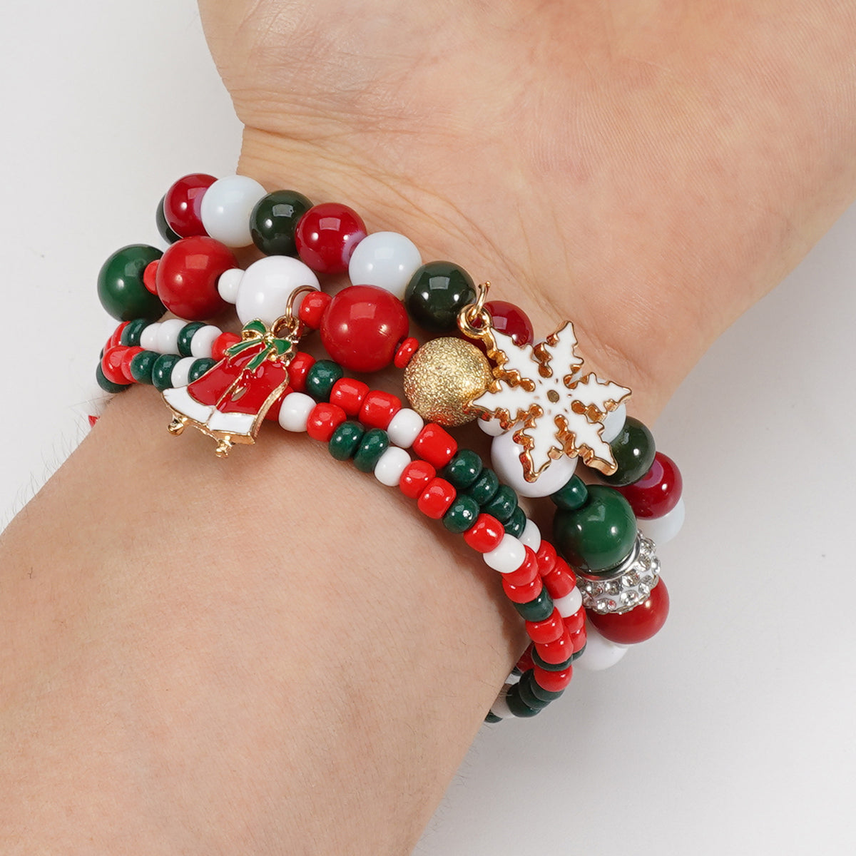 Wrist wearing a stack of red, green and white bead stretch bracelets with snowflake and bell charms