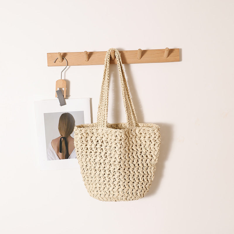 Beige paper straw shoulder bag with braided straps hanging on a wooden peg rack
