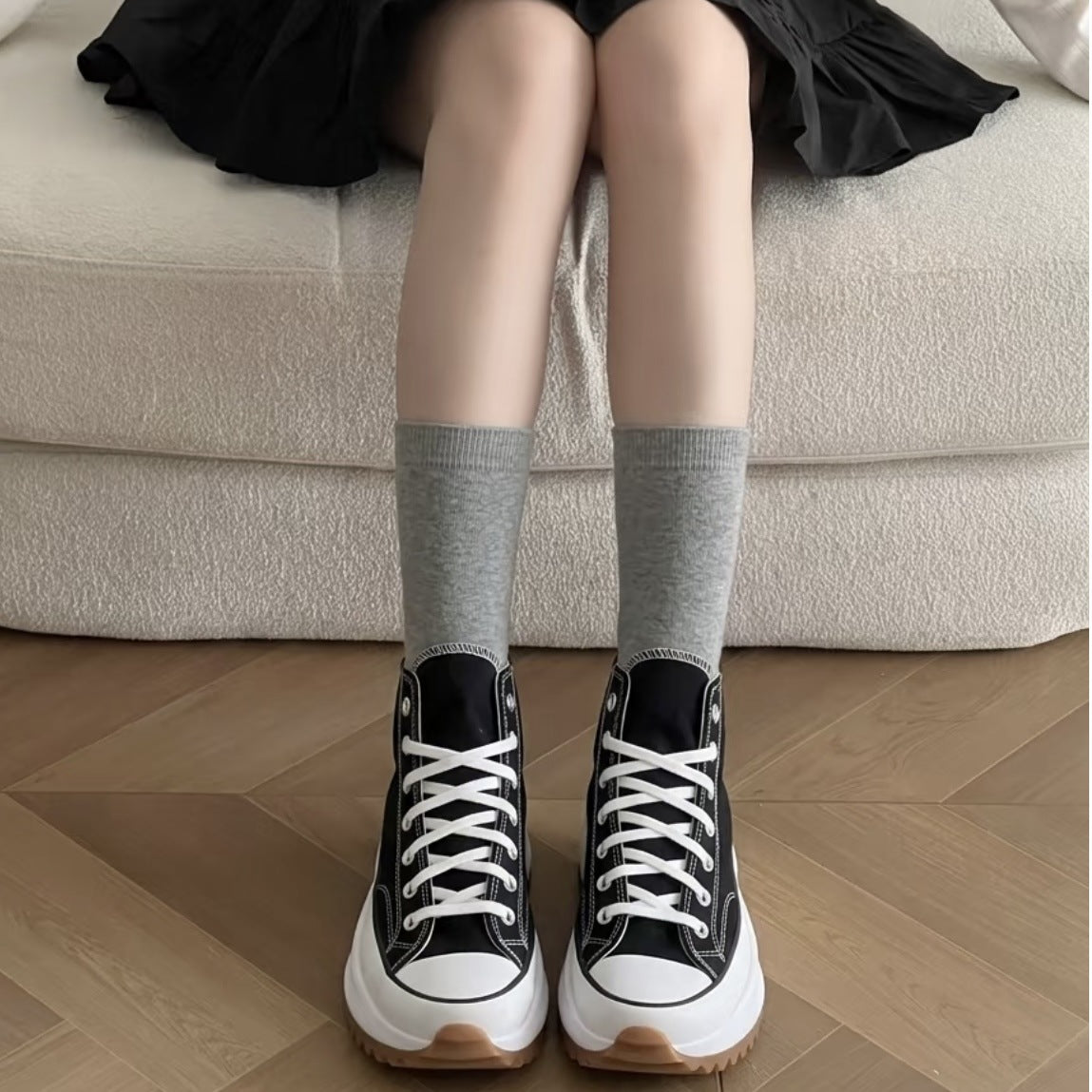 Black high-top platform canvas sneakers with white laces seen from the front on a parquet floor with gray socks