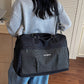 Black travel duffel with a grid front pocket worn crossbody on the back over a gray sweater