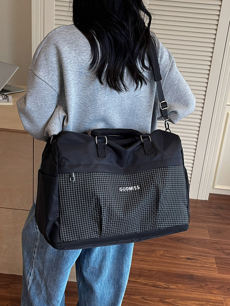 Black travel duffel with a grid front pocket worn crossbody on the back over a gray sweater