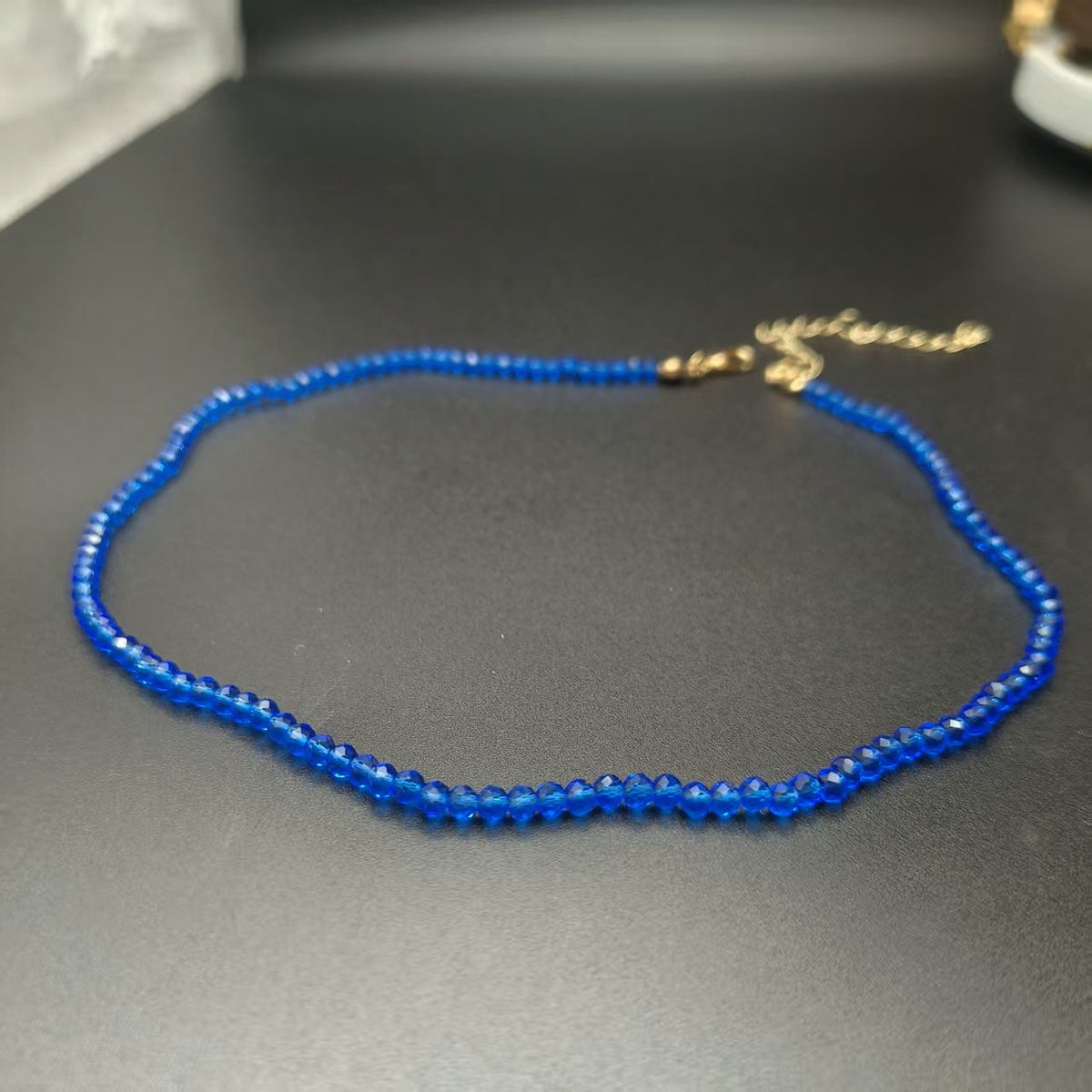 Faceted glass bead choker necklace with a gold tone chain on a plain background