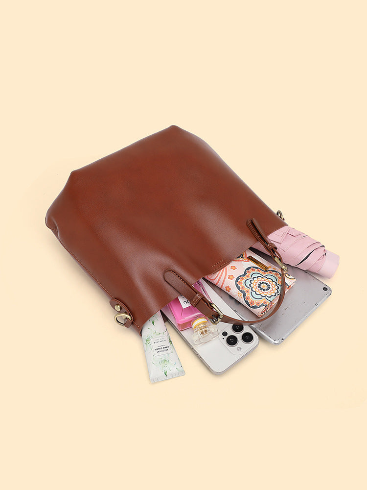 Chestnut brown leather bucket tote lying on its side with a phone, a pouch and small items beside it