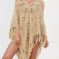Tassel fringe knit poncho in soft acrylic yarn draped over a fitted top and jeans