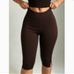 Woman in brown high-waisted slim-fit capri leggings with hands at the waistband, front view