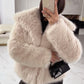 Woman in a pale beige vegan fur jacket taking a mirror selfie in black trousers with a small black bag