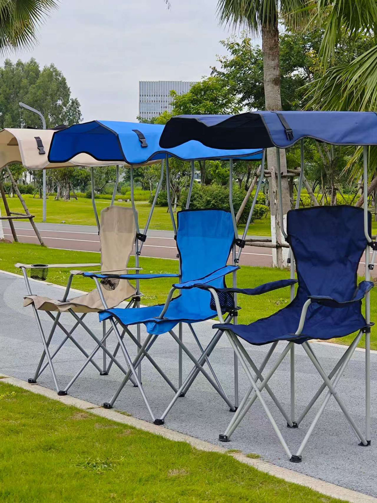 Beige, blue and navy foldable camping chairs with canopies seen from the side on a park path