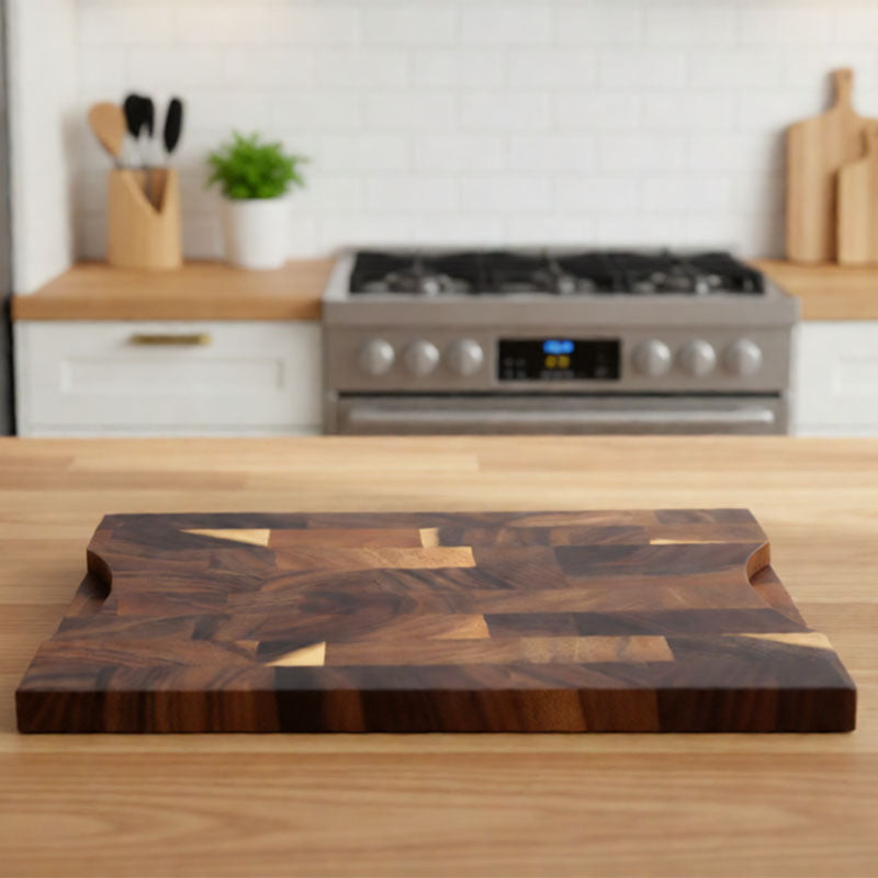 Walnut cutting board on a wood counter with carved grip cutouts on its short side