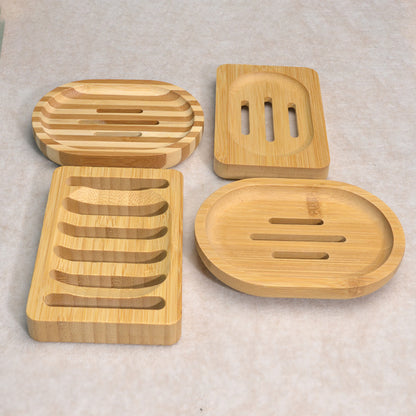 Four natural bamboo soap dishes in different shapes on a light tan surface