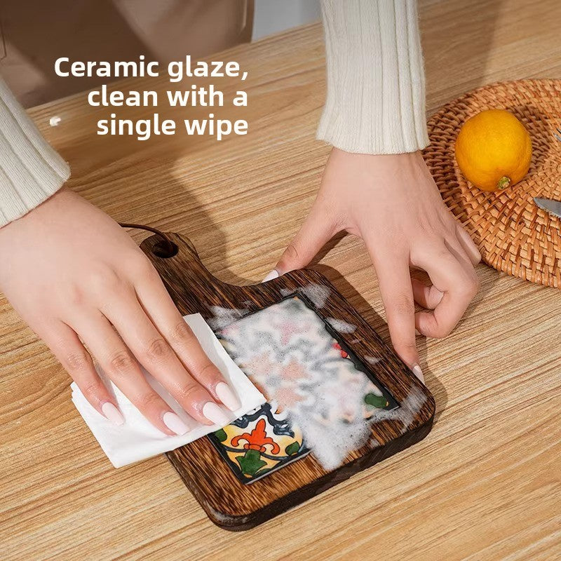 Hands wiping the glazed ceramic tile of a dark wooden trivet with a white tissue