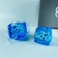 Clear blue gel ice cube squishy toy held up to the light with drifting white snowflakes