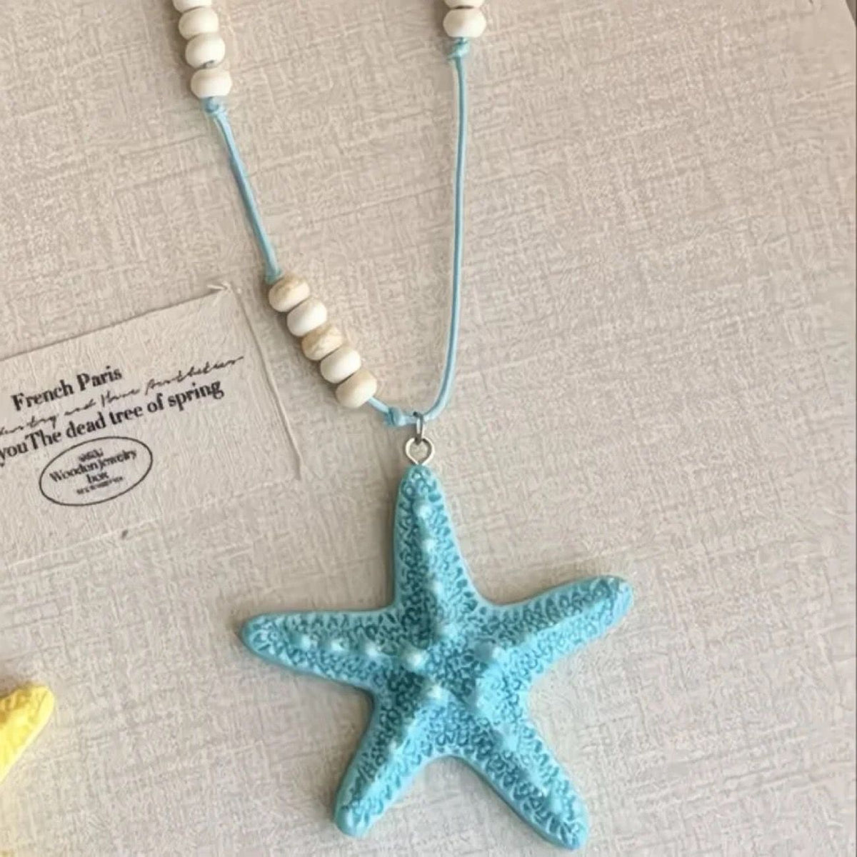 Blue resin starfish pendant on a sky-blue cord with pale wood-tone beads on a textured surface