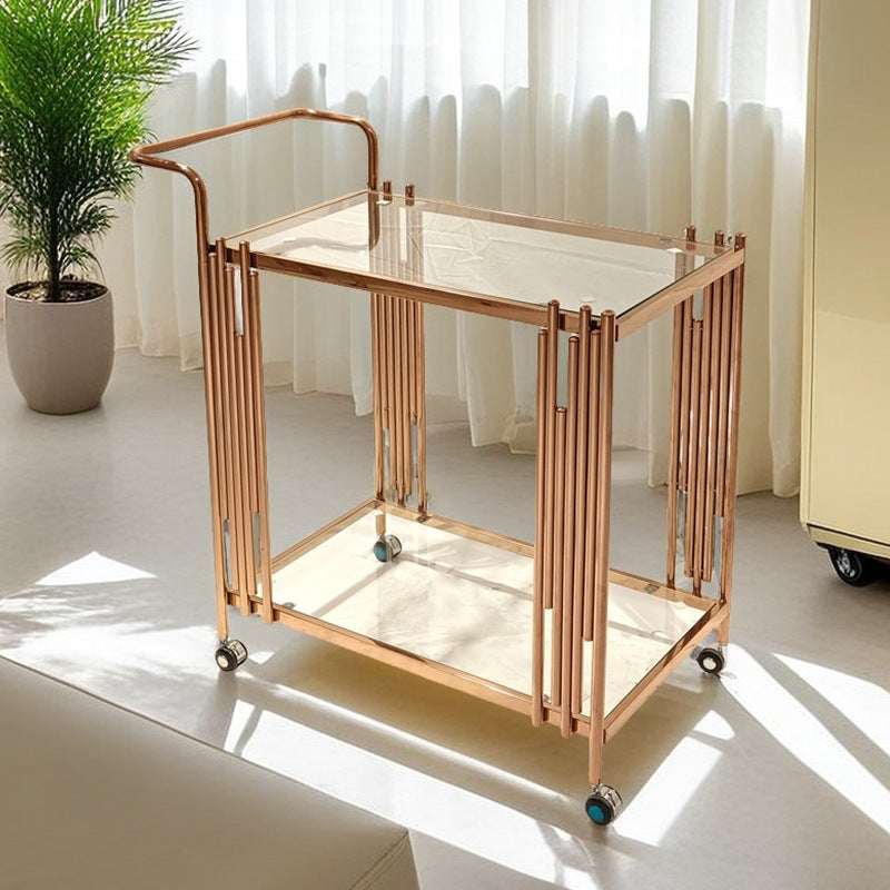 Gold toned stainless steel two tier serving cart with tempered glass shelves in a living room