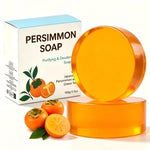 Round amber persimmon soap bar leaning on a stacked bar beside a Persimmon Soap box and fresh persimmons