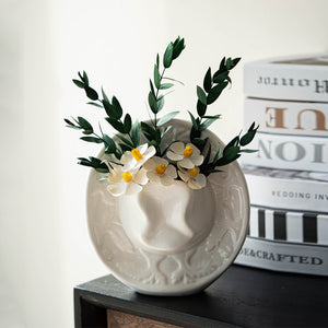 White glazed ceramic cowboy hat vase holding daisies and eucalyptus on a dark shelf