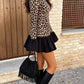 Side view of a leopard print long sleeve mini dress with a black ruffle hem and a black fringed bag