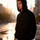 Man wearing an oversized black pullover hoodie with the hood up on a city street