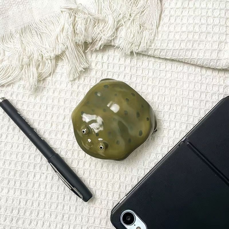 Plain olive resin frog earbud case seen from above on white cloth beside a pen and a tablet