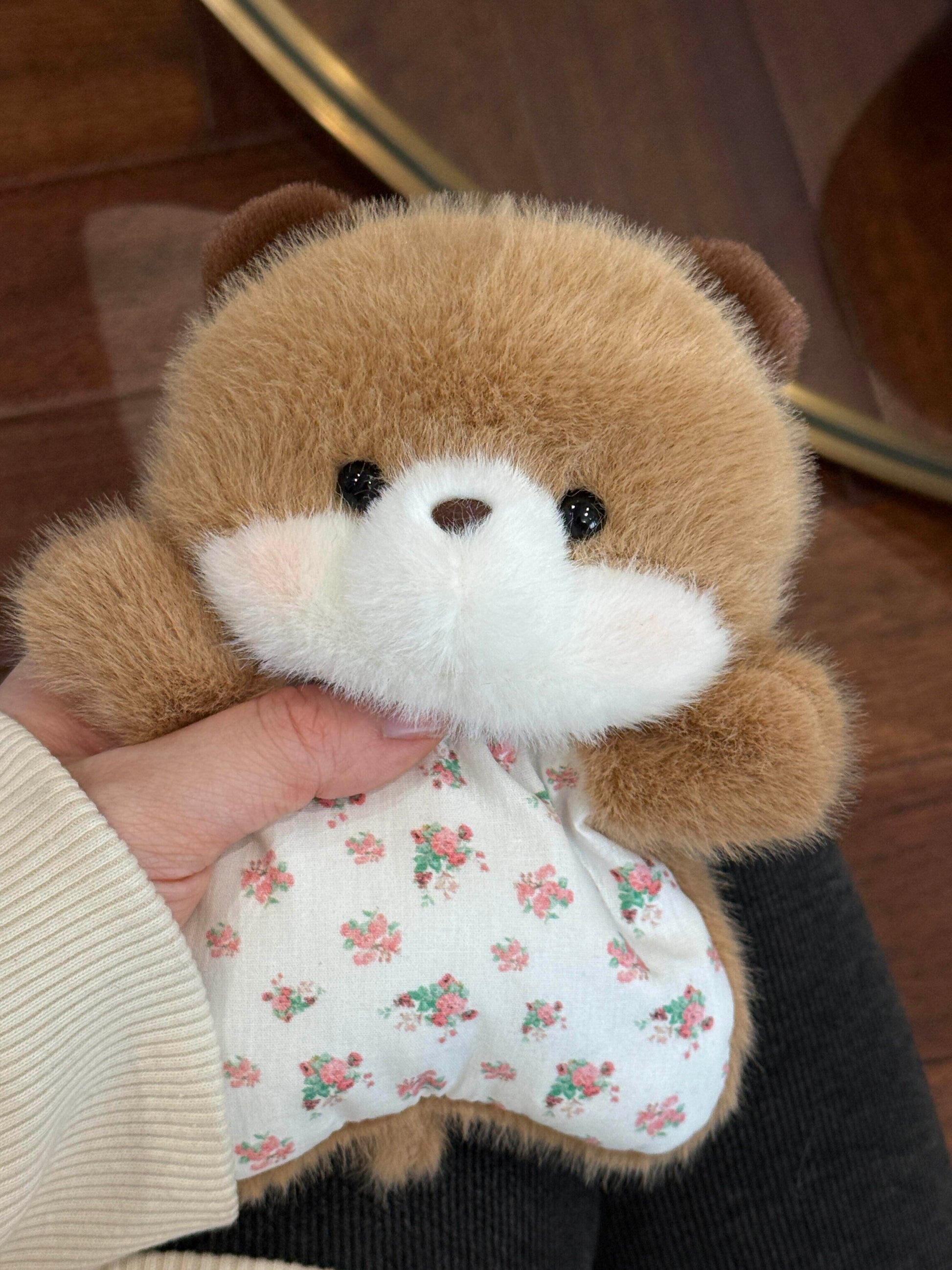 Brown plush bear squishy bean bag toy held in hand, round face and pink floral cotton apron