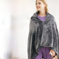 Woman in the dark gray flannel heating shawl with a center zip and a cord with a small controller held in her hand