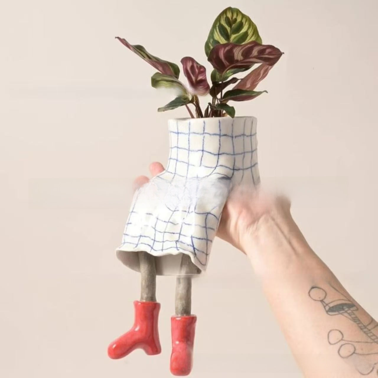 Resin lower body planter in a blue grid skirt and red boots holding a plant