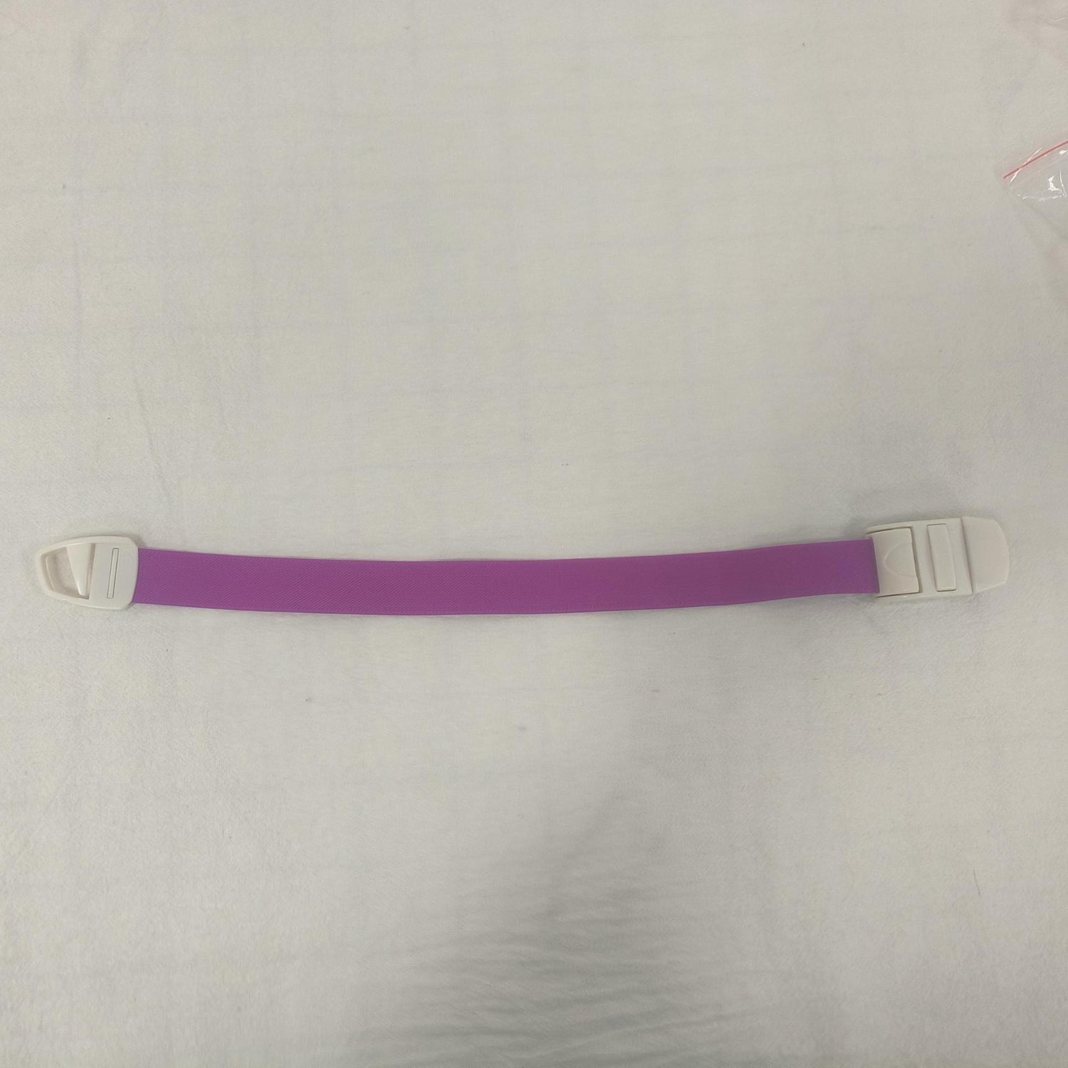 Single purple elastic quick release tourniquet band with a white snap buckle laid flat