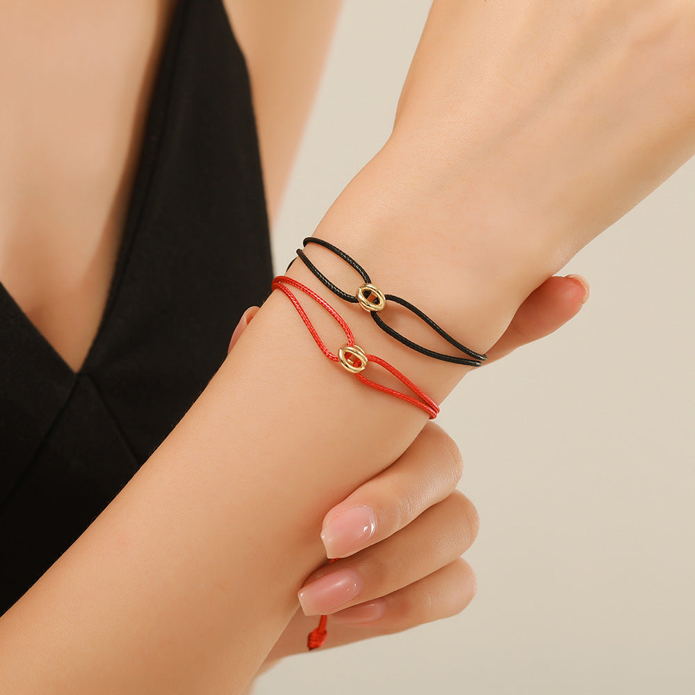 Red cord lucky charm bracelet with a gold charm worn on a womans wrist