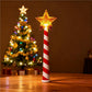 Glowing star Christmas wand stood on a table beside a lit tree, candy cane striped handle