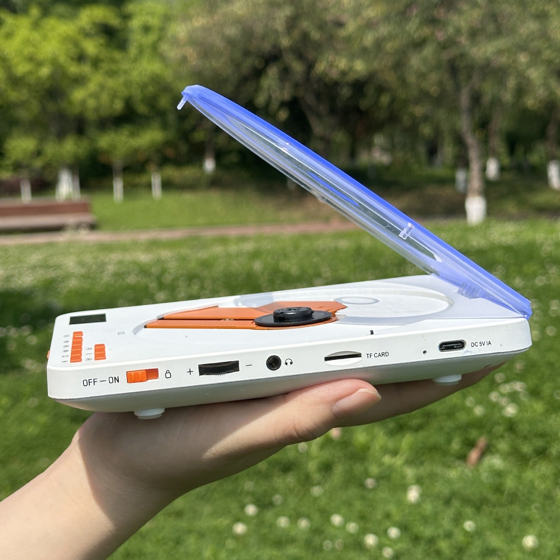 Clear lid portable CD player held in one hand showing the side ports outdoors