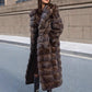 Woman in a long brown banded fur coat worn open over a printed dress and black boots on a city street