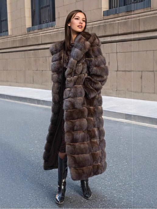 Woman in a long brown banded fur coat worn open over a printed dress and black boots on a city street
