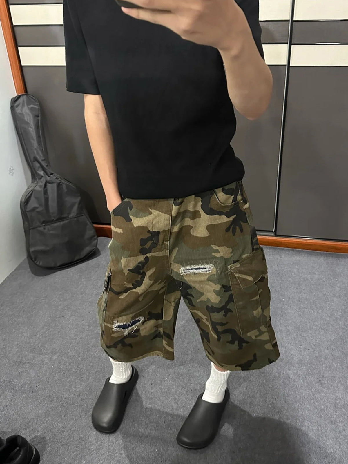 Camo ripped denim cargo shorts worn with white socks and black clogs, side cargo pocket and torn window visible