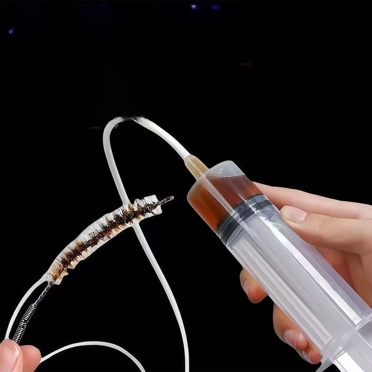 Hand pushing a flexible tube into a drain hole while holding a syringe of brown water