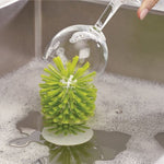 Green suction base cup brush cleaning the inside of a wine glass in a soapy sink