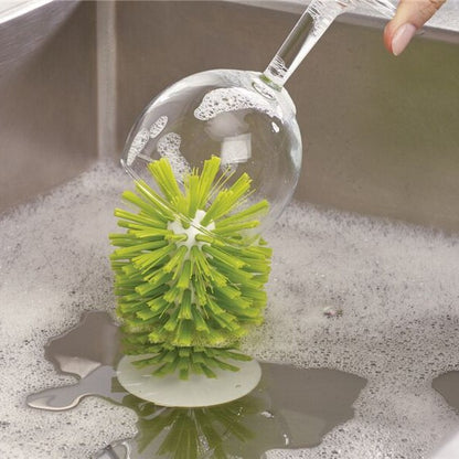 Green suction base cup brush cleaning the inside of a wine glass in a soapy sink