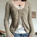 Woman wearing the khaki cable knit cardigan over a white lace camisole and jeans, front view