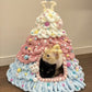 Pink, blue and white chenille tree shaped pet house with two cats looking out of the arched doorway