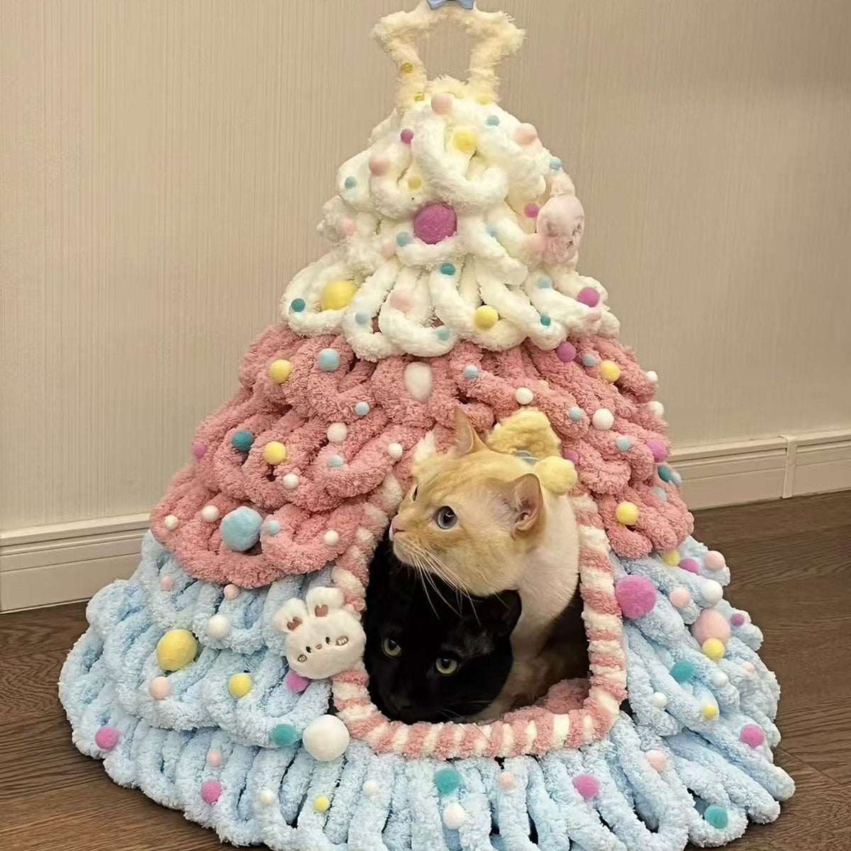 Pink, blue and white chenille tree shaped pet house with two cats looking out of the arched doorway