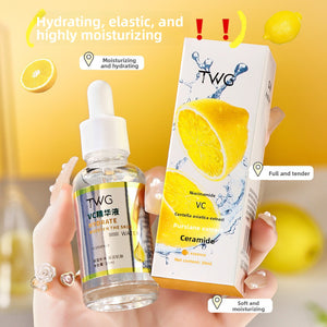 Hand holding a clear TWG VC essence dropper bottle beside its lemon print carton