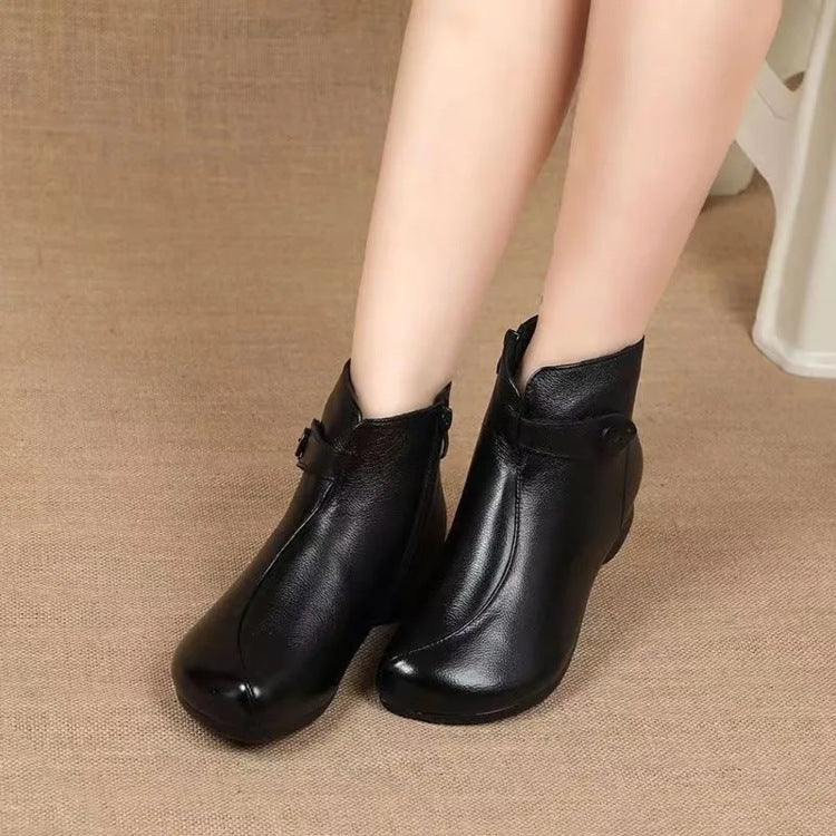 Woman's legs in black soft leather ankle boots with a side strap on a woven background