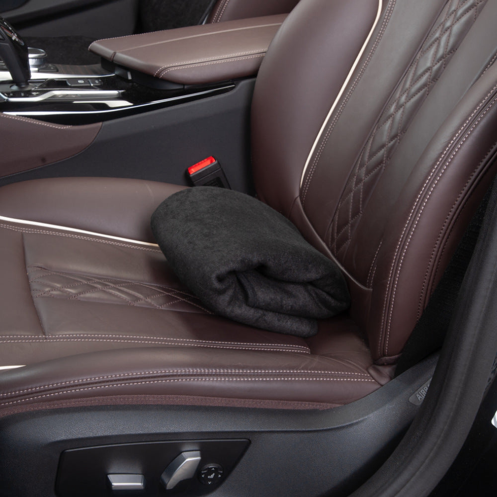 Black terry cloth seat cover folded flat on a brown leather car seat, showing its compact folded size