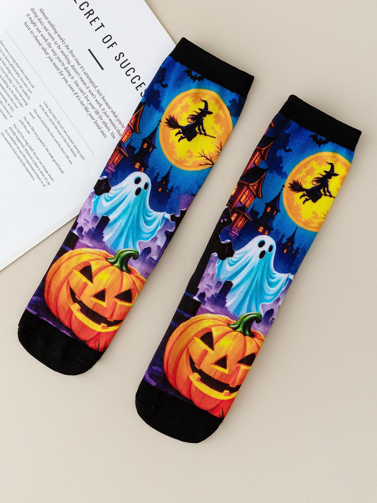 Pair of mid-calf socks printed with a ghost, a witch on a broom across a yellow moon and two pumpkins