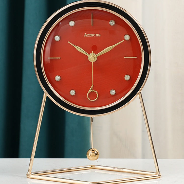 Orange dial desk clock with black bezel and gold hands on a triangular gold stand with a swinging gold ball, teal curtain