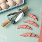 Stainless steel croissant roller cutter with wooden handle on a dough mat beside cut croissant dough pieces