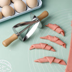 Stainless steel croissant roller cutter with wooden handle on a dough mat beside cut croissant dough pieces